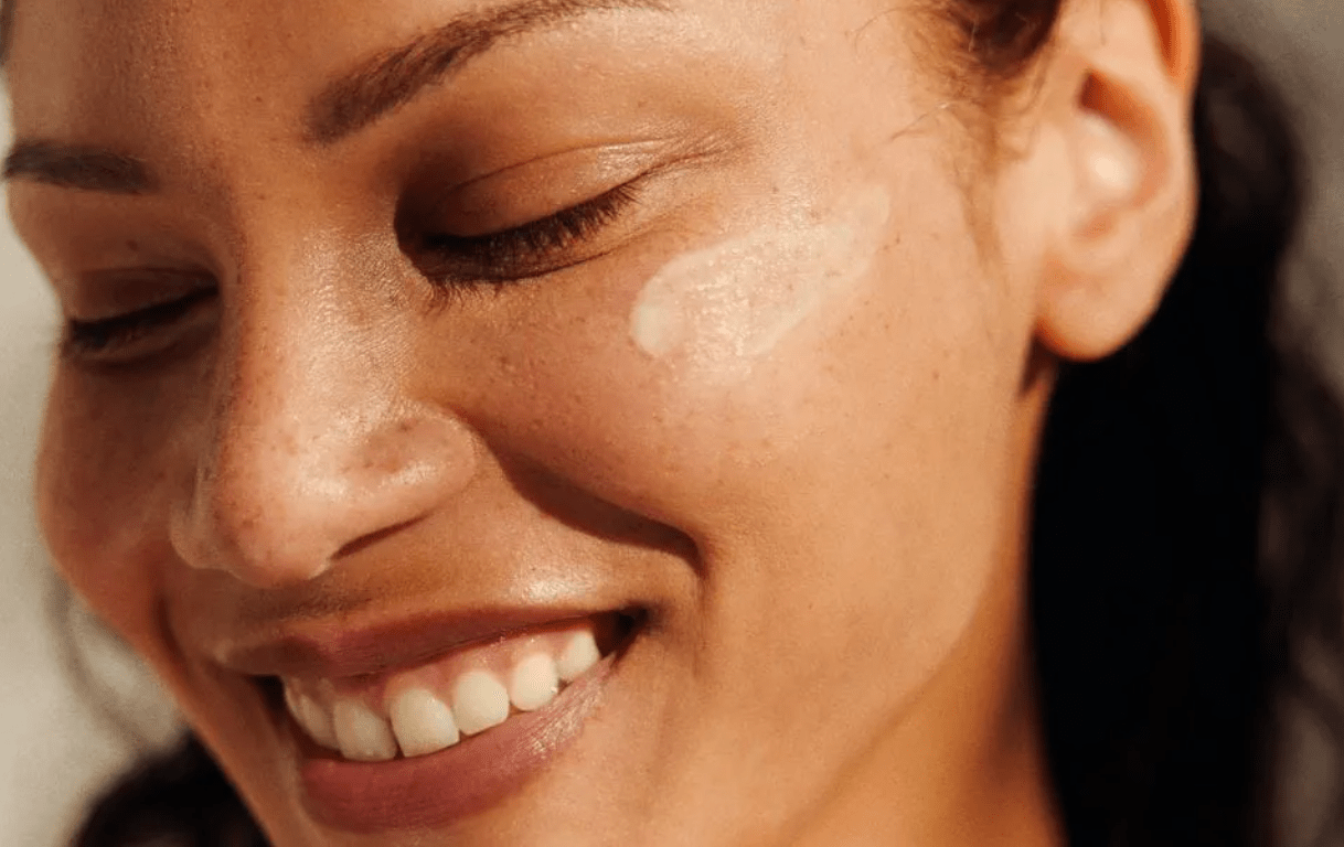 Close-up of a smiling woman with smooth, radiant skin and a swipe of Rzn-A-Bull Tallow Balm on her cheek. The rich, nutrient-dense balm blends effortlessly, providing deep hydration and skin barrier support. Ideal for sensitive, dry, or irritated skin. Natural skincare made with regeneratively sourced, grass-fed tallow for long-lasting moisture.
